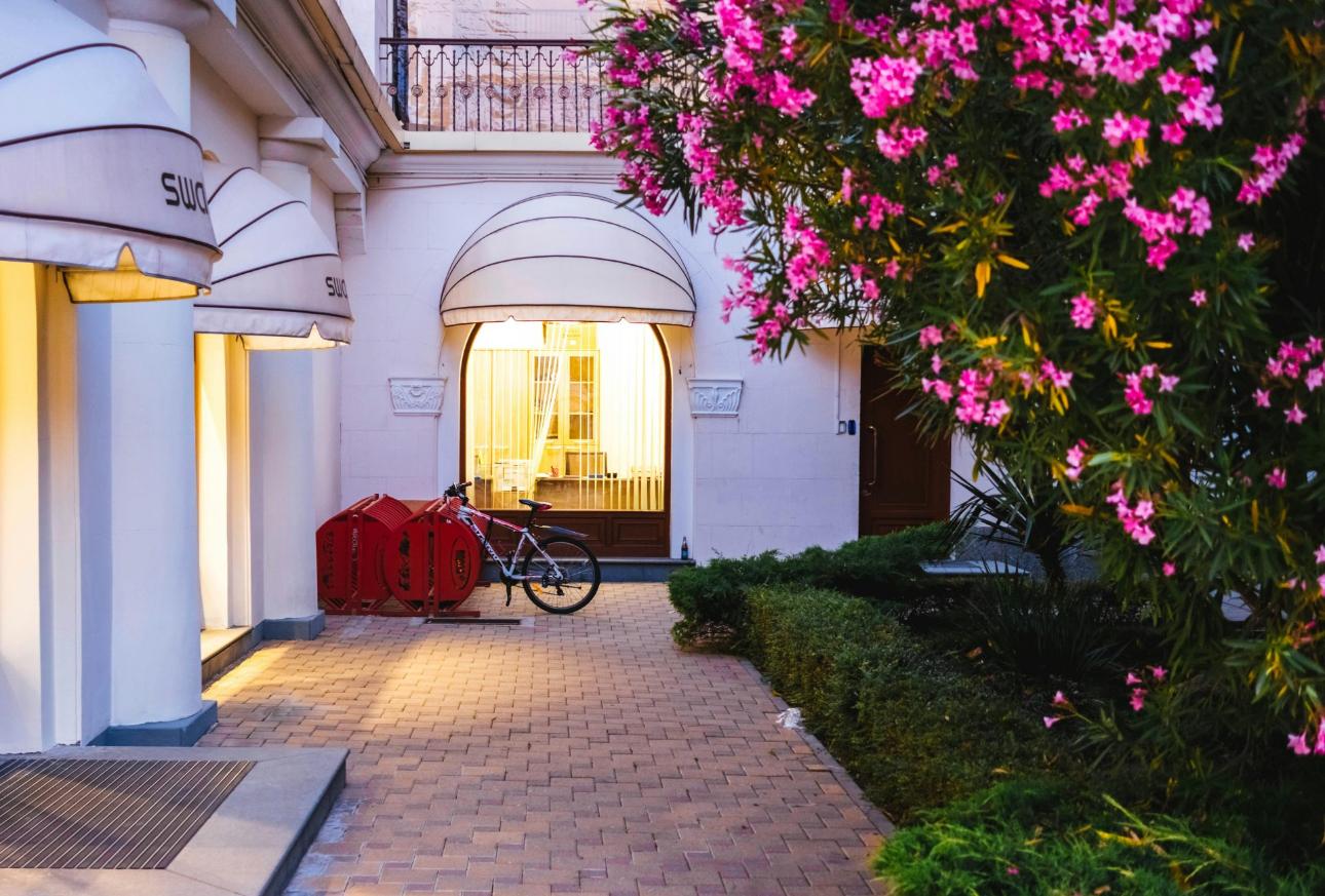 Vue sereine du soir sur l'entrée d'un hôtel-boutique à Sotchi, ornée de fleurs vibrantes et d'un éclairage chaleureux.