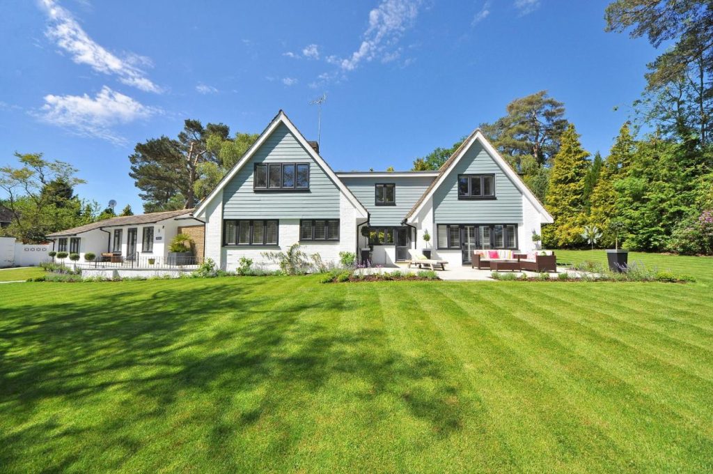 Extérieur d'une maison familiale moderne présentant une grande pelouse et un jardin sous un ciel bleu clair.
