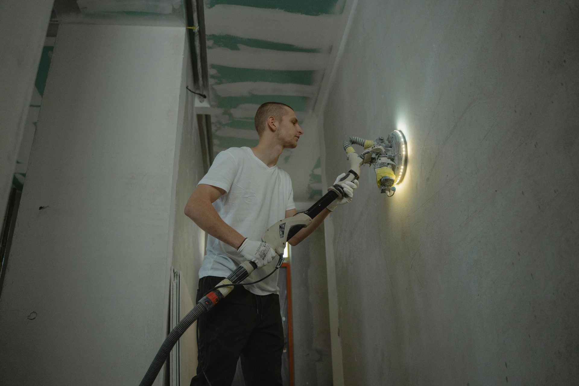 Un homme ponce un mur intérieur avec un outil de ponçage automatique lors de travaux de rénovation à l'intérieur.