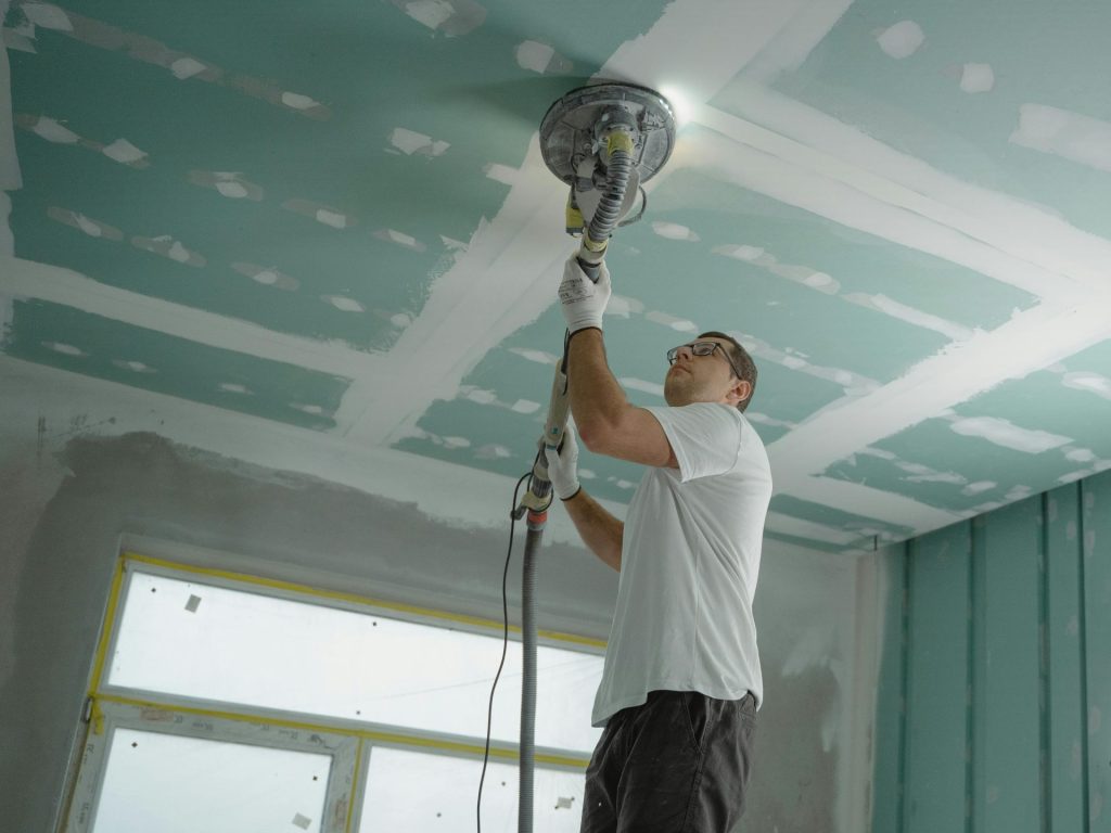 Un ouvrier professionnel ponce le plafond lors d'un projet de rénovation. Construction intérieure.