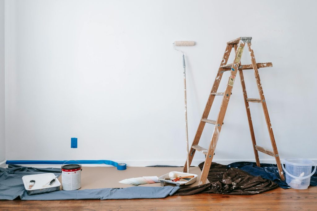 Une pièce préparée pour la rénovation avec une échelle, des fournitures de peinture et une toile de protection.
